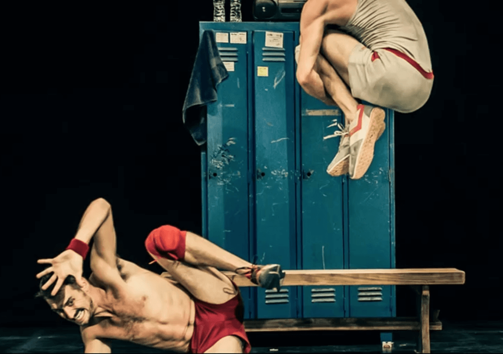 Two male performers mid-air in choreographed leap, Un Poyo Rojo.